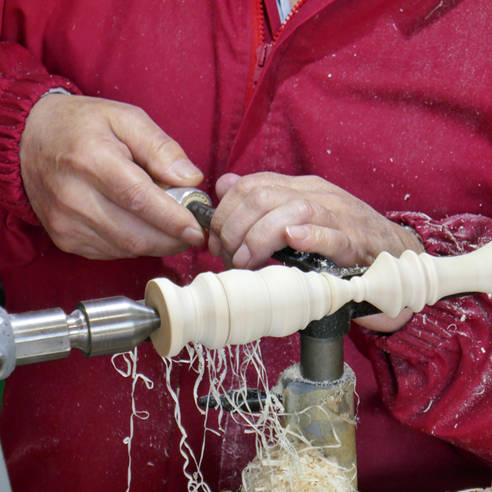 unas manos manejan una gubia y tallan en torno de madera una pieza