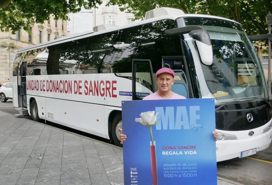 un hombre sujeta el cartel de la campaña de donación de sangre en el MAE frente a la unidad movil de extracción de sangre