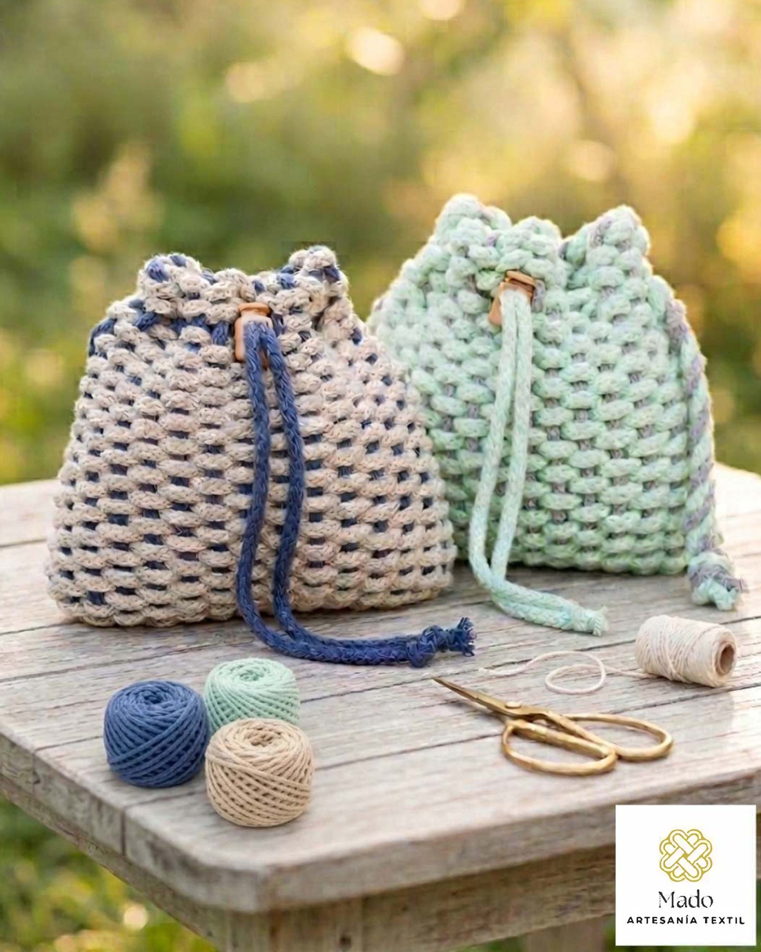 Bolso de mano Dos bolsos de mano de macramé tejido con cordones, tijeras de costura y el logotipo de Mado Artesanía Textil.