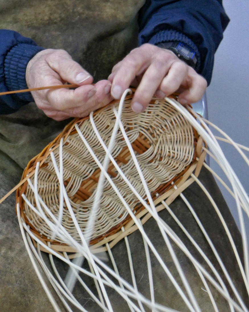cestería con Ramon Vázquez Un primer plano de las manos de un artesano tejiendo una cesta de mimbre de forma ovalada,